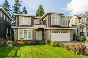Ein zweistöckiges Haus mit Garage, einem gepflegten Rasen und verschiedenen Sträuchern und Blumen.