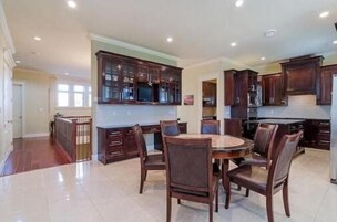 A spacious kitchen with dark wooden cabinets, a dining table with chairs, and a tiled floor.