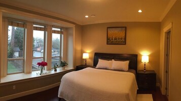 A bedroom with a large bed, two bedside lamps, a window with a view, and a painting on the wall.
