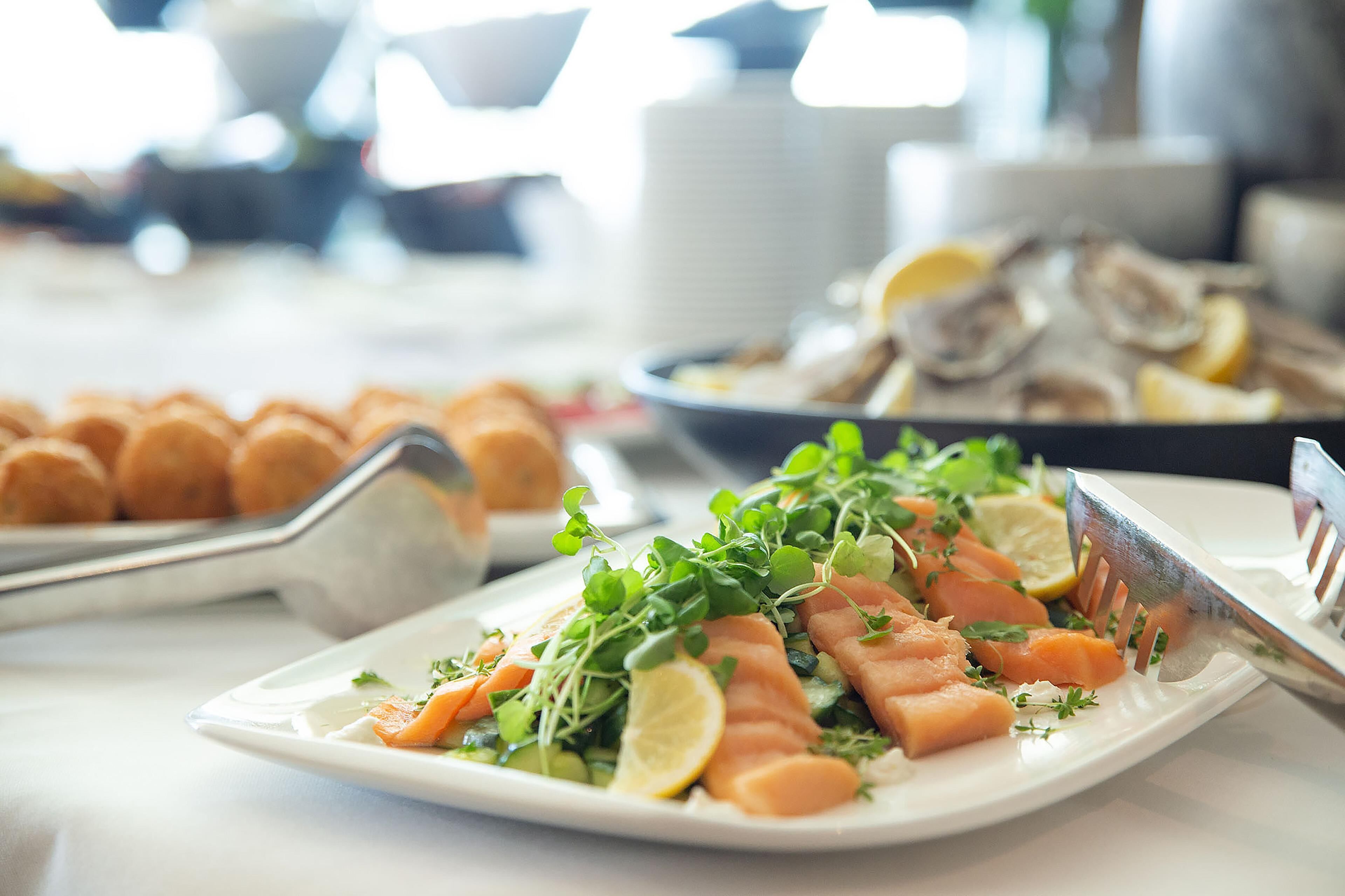 A buffet table with various dishes including salmon, lemon slices, and greens.