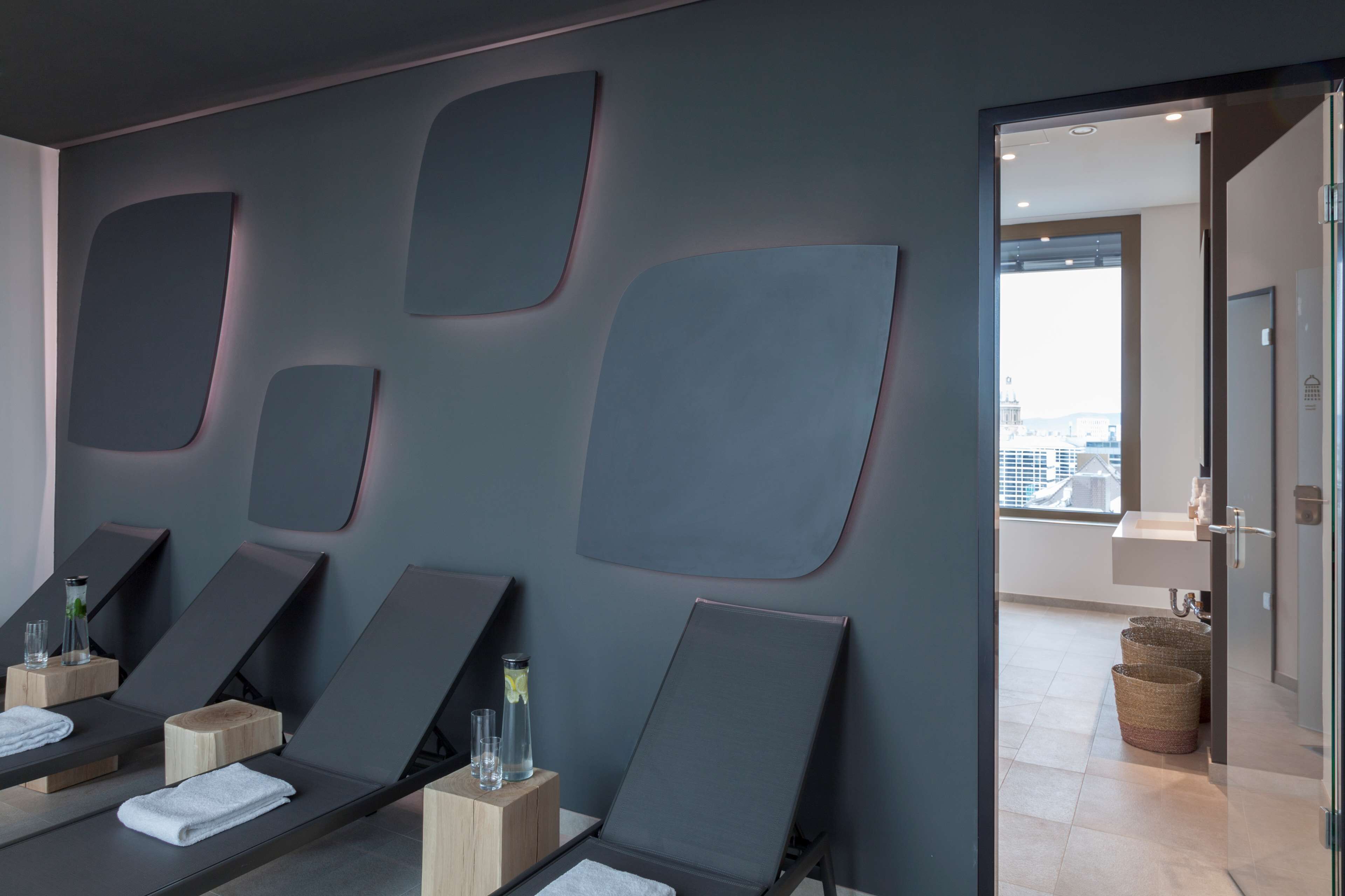 Een moderne spa met ligstoelen, een groot raam en uitzicht op de stad.