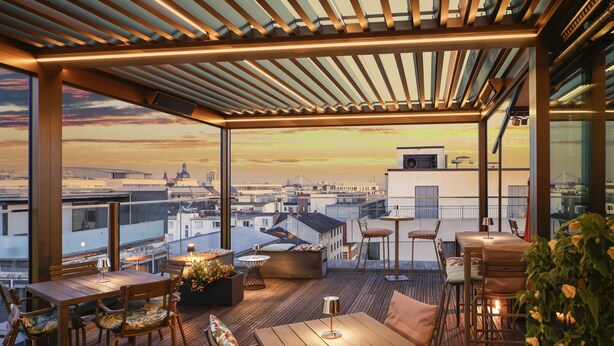 A rooftop terrace with wooden flooring, tables, chairs, and a view of the city skyline at sunset. - Radisson Blu Hotel, Mannheim (Mannheim)