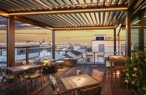 A rooftop terrace with wooden flooring, tables, chairs, and a view of the city skyline at sunset. - Radisson Blu Hotel, Mannheim (Mannheim)