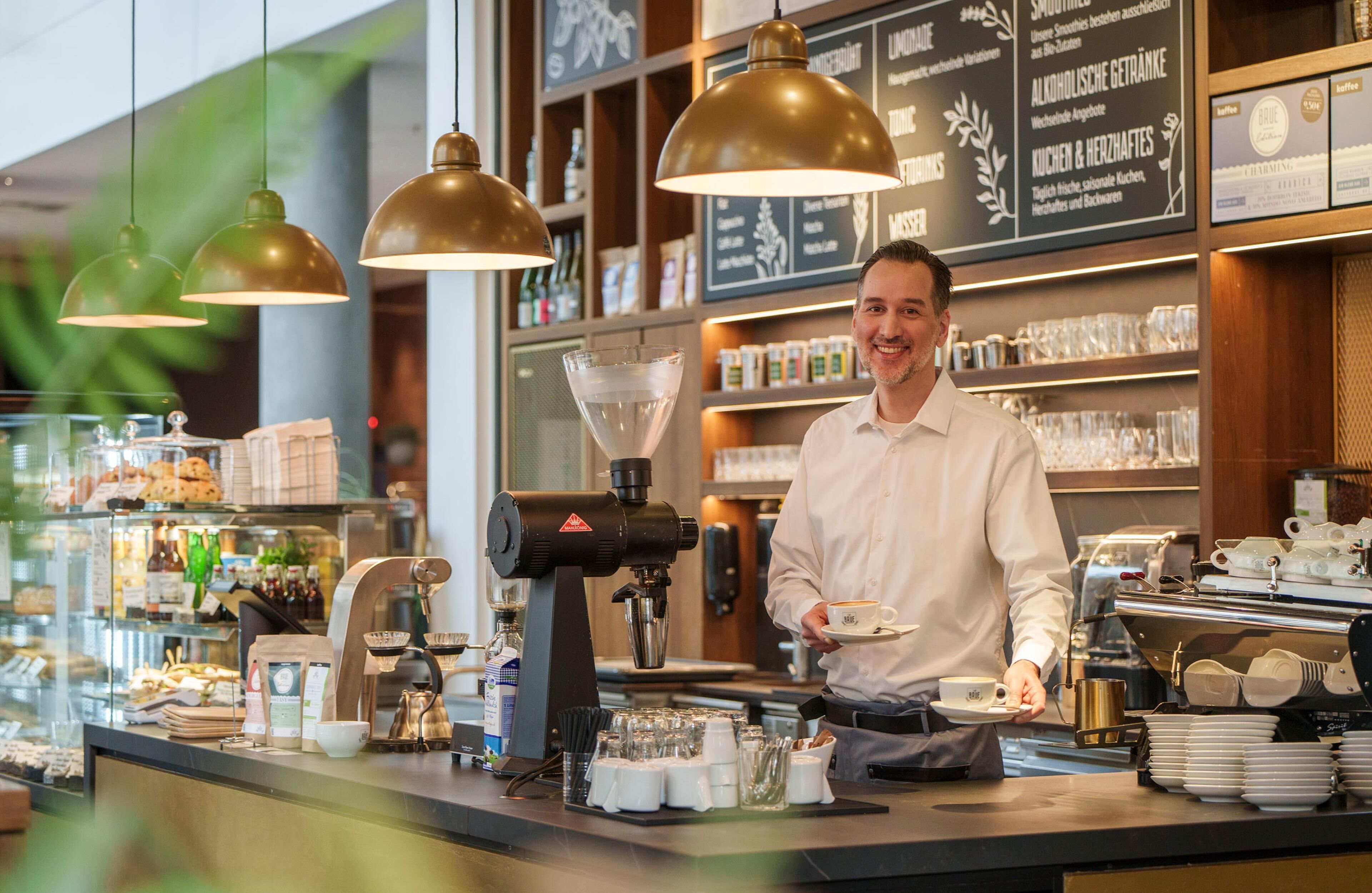 A coffee shop counter with a coffee machine, cups, and a menu board in the background.