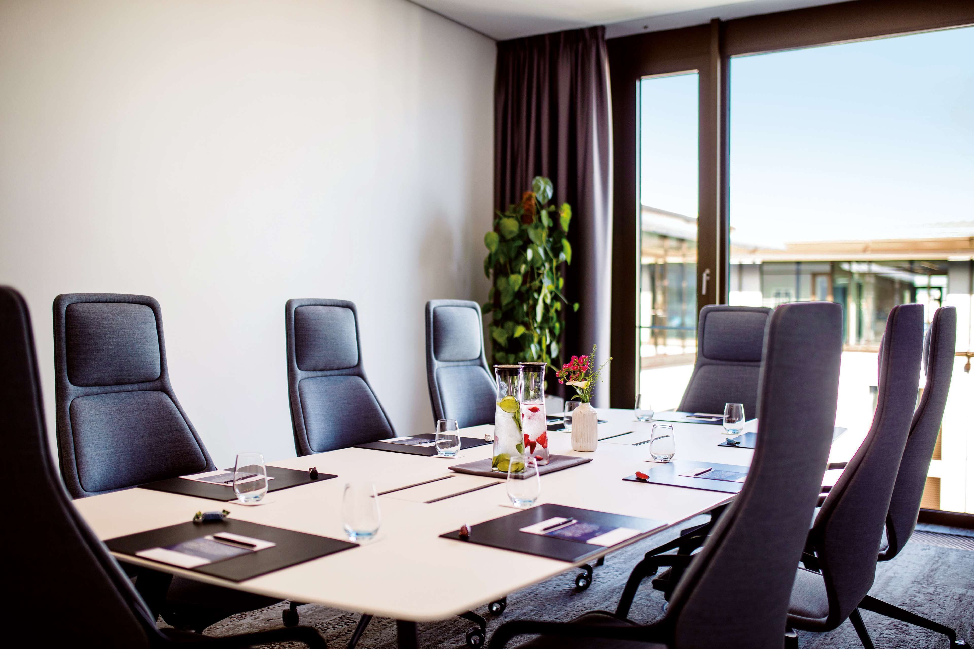 A conference room with a large table, multiple chairs, water glasses, and a vase with flowers.