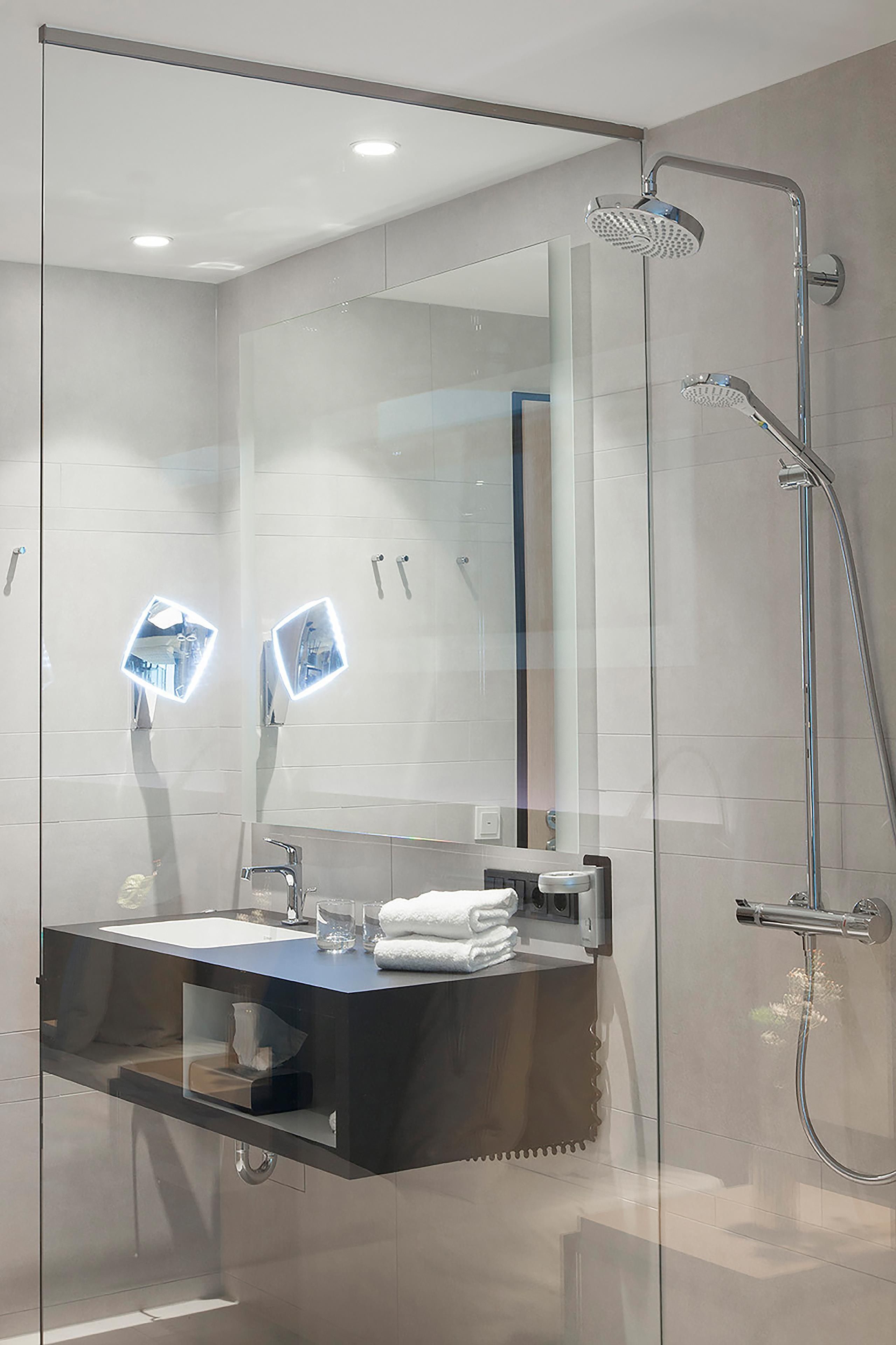 Ein modernes Badezimmer mit einer Duschkabine aus Glas, einem Waschtisch mit Spiegel und einem Waschbecken.