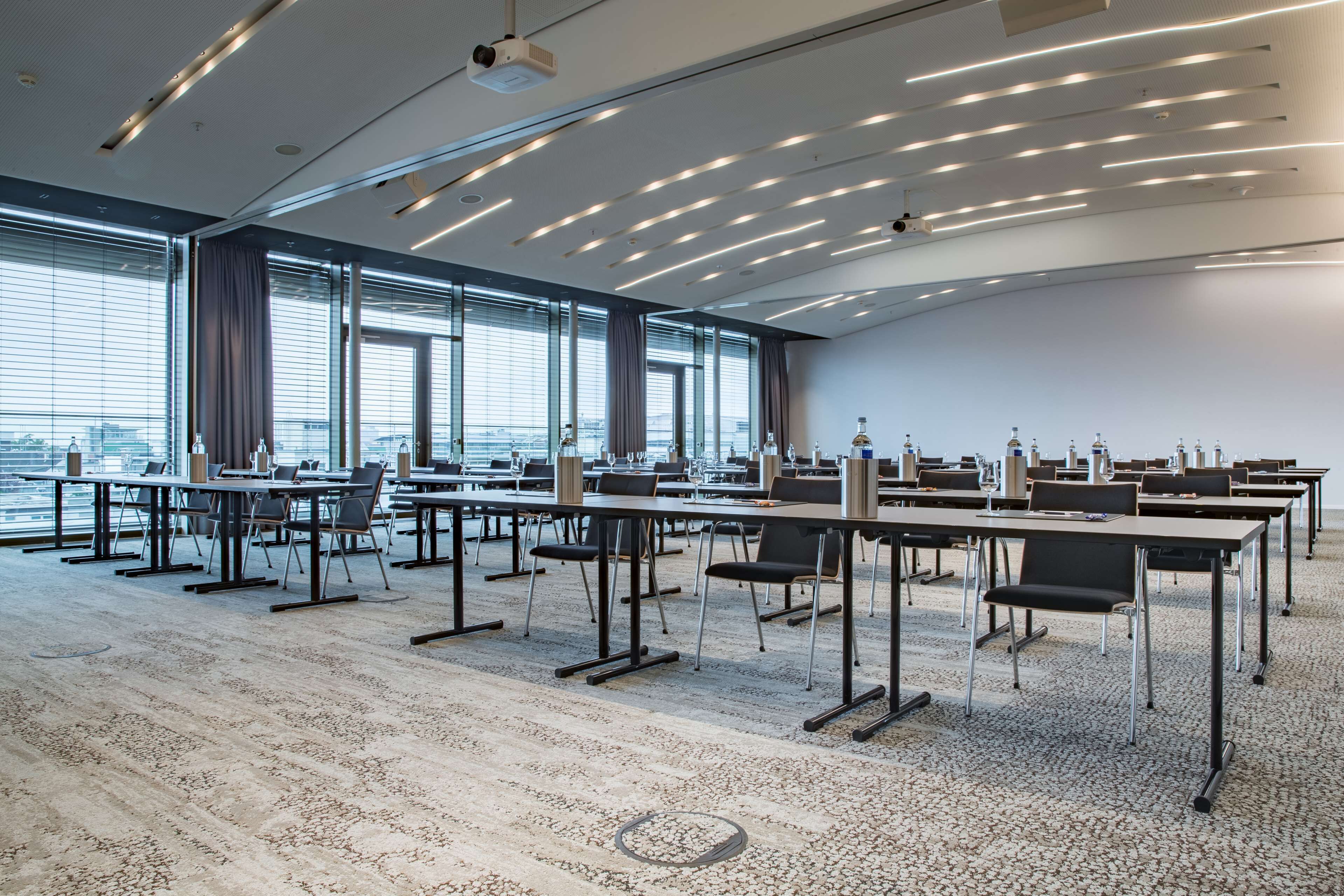 A conference room with multiple tables and chairs, large windows, and a view of the cityscape.