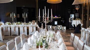 A banquet hall with round tables set for a formal event, featuring white tablecloths, neatly arranged chairs, and elegant lighting fixtures.