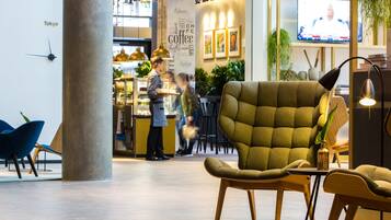 A modern interior with a large green armchair, a coffee shop in the background, and a clock on the wall.