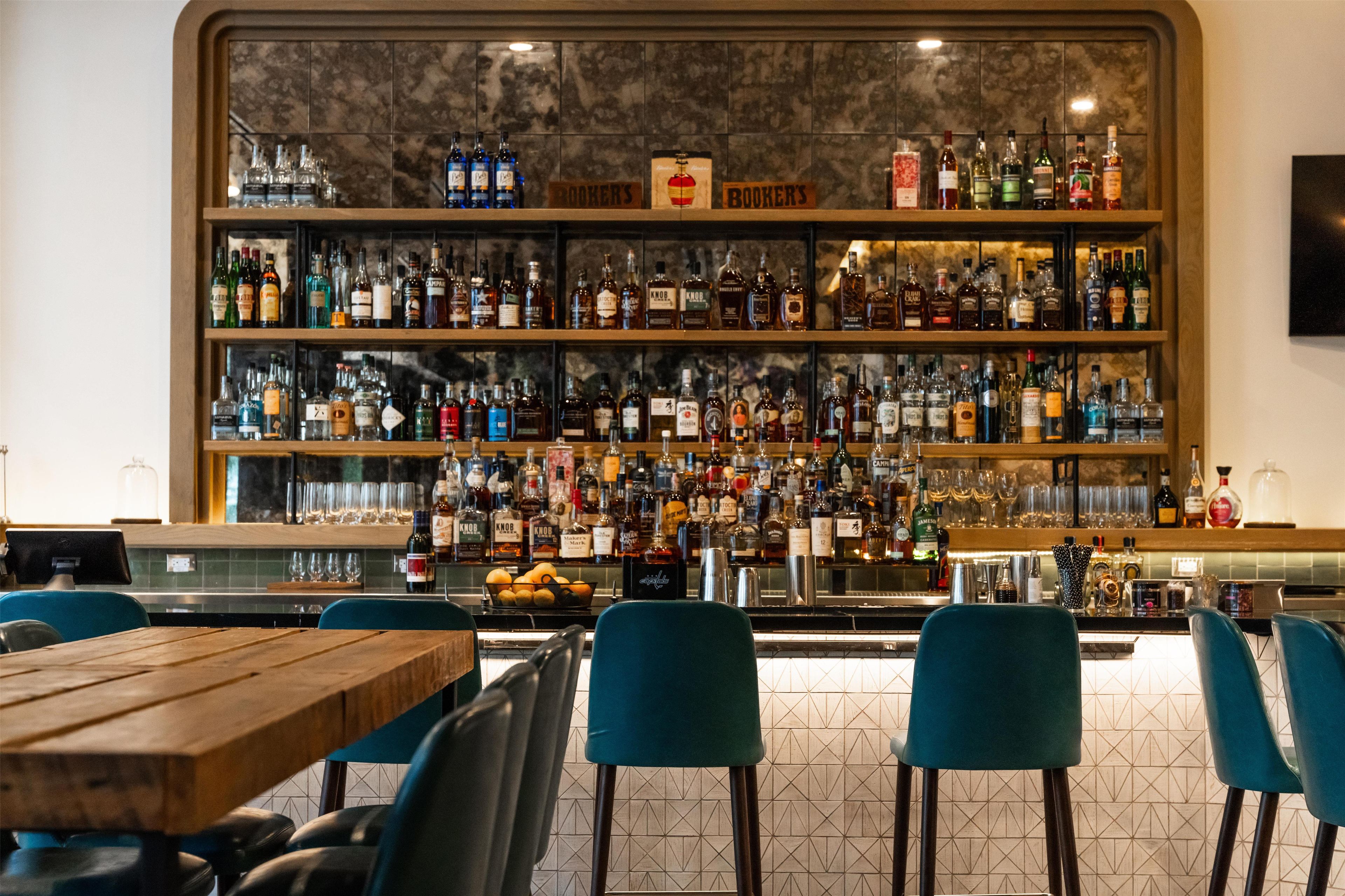 Un espace bar doté de plusieurs étagères remplies de bouteilles d’alcool, d’un saladier de fruits et de tabourets de bar.