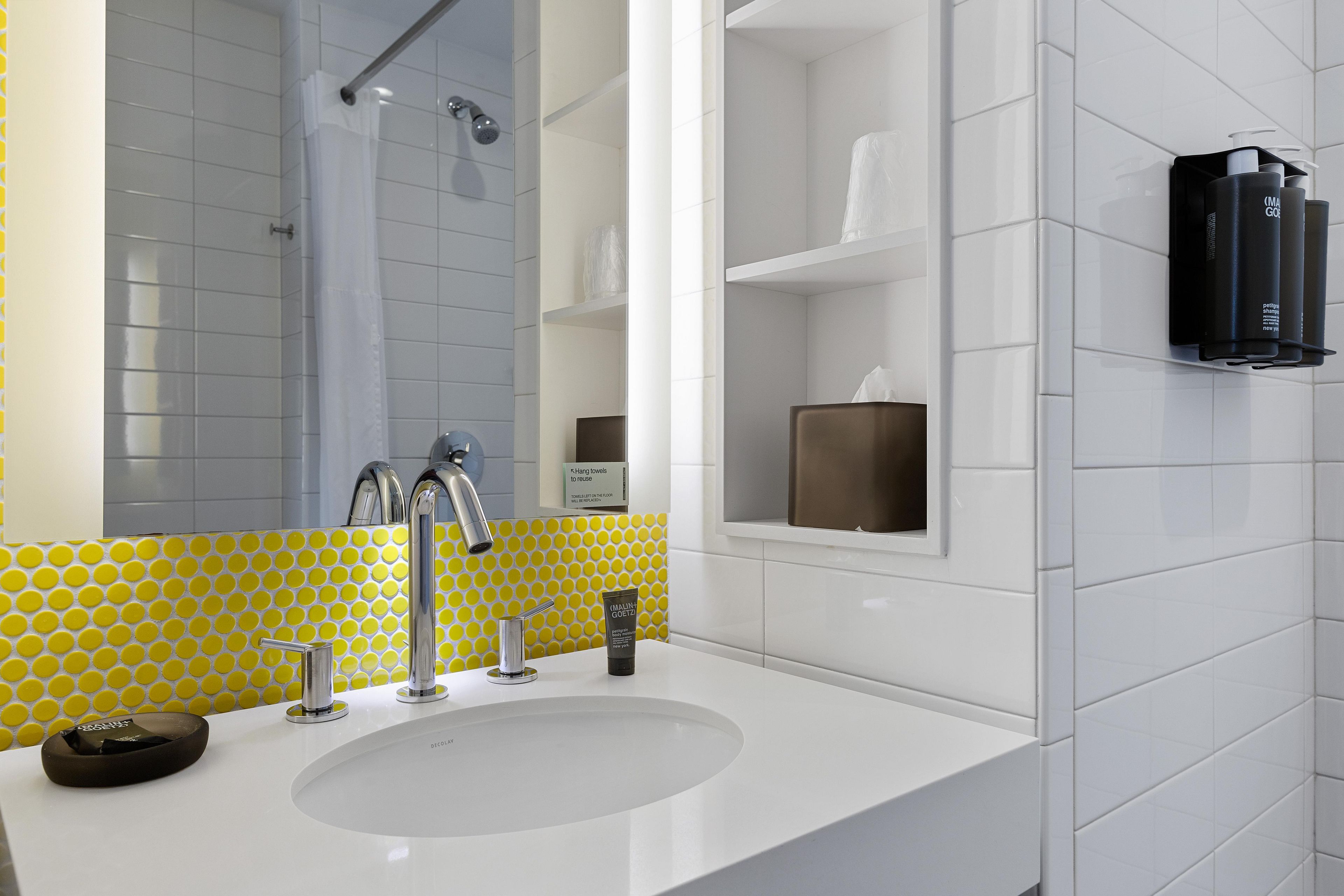 A modern bathroom with a white sink, chrome faucets, and a yellow polka dot tile backsplash.