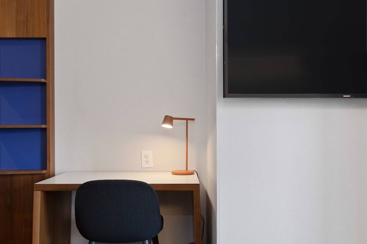 Ein Schreibtisch mit Lampe, ein Stuhl und ein an der Wand montierter Fernseher.