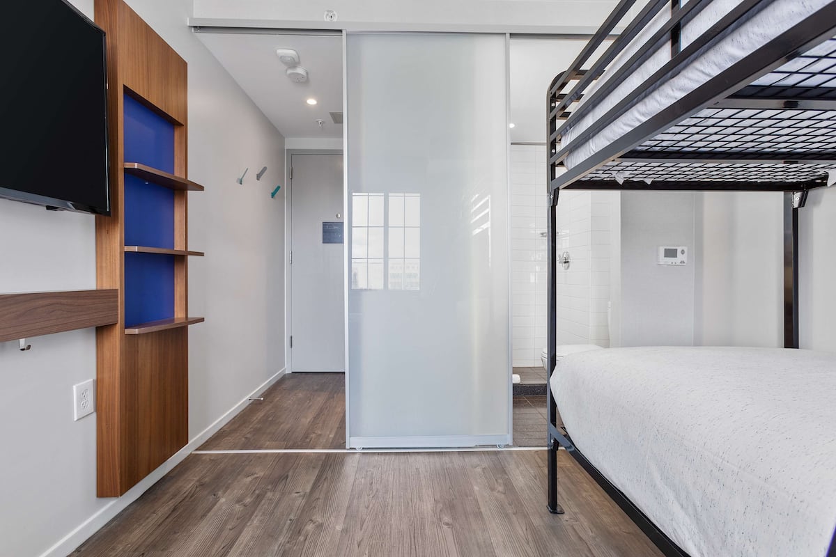 Ein modernes Hotelzimmer mit Etagenbett, Flachbildfernseher und einer Schiebetür zu einem Badezimmer.
