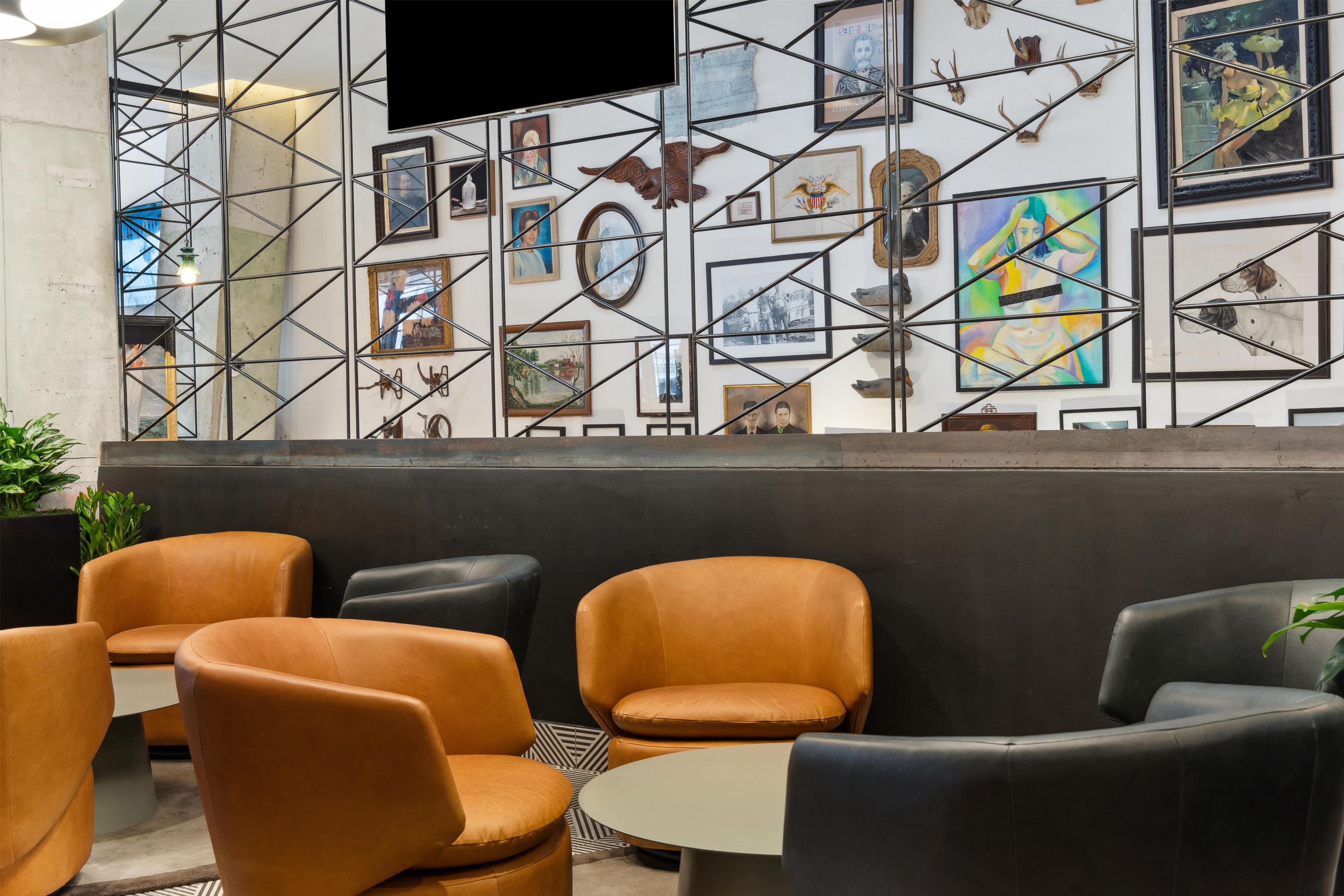 Un área de estar con sillones de cuero y una mesa redonda, una pared con obras de arte enmarcadas y elementos decorativos, y un televisor montado en la pared.