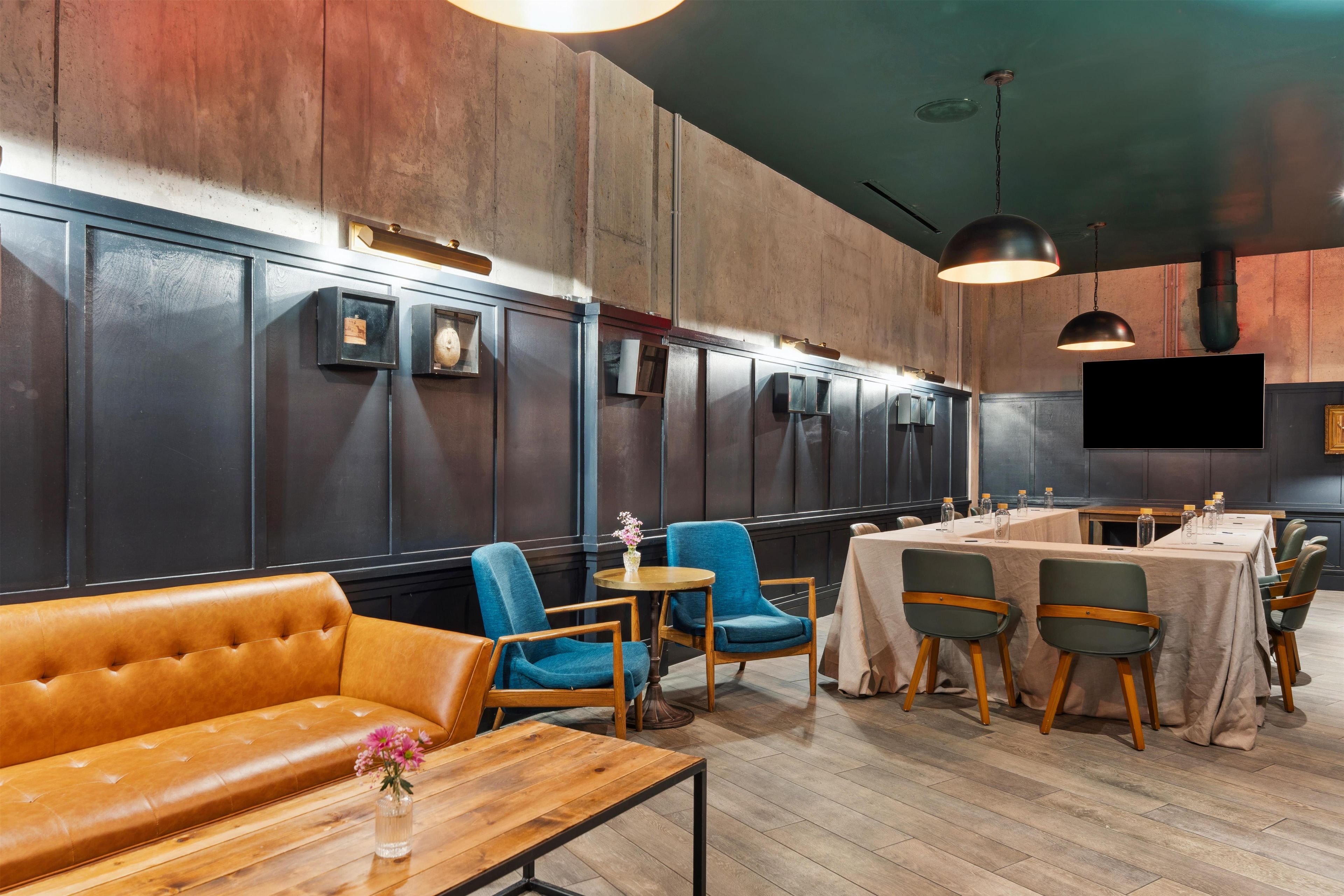 Interior de un restaurante con una barra larga, sillas azules, un sofá de cuero y un televisor montado en la pared.