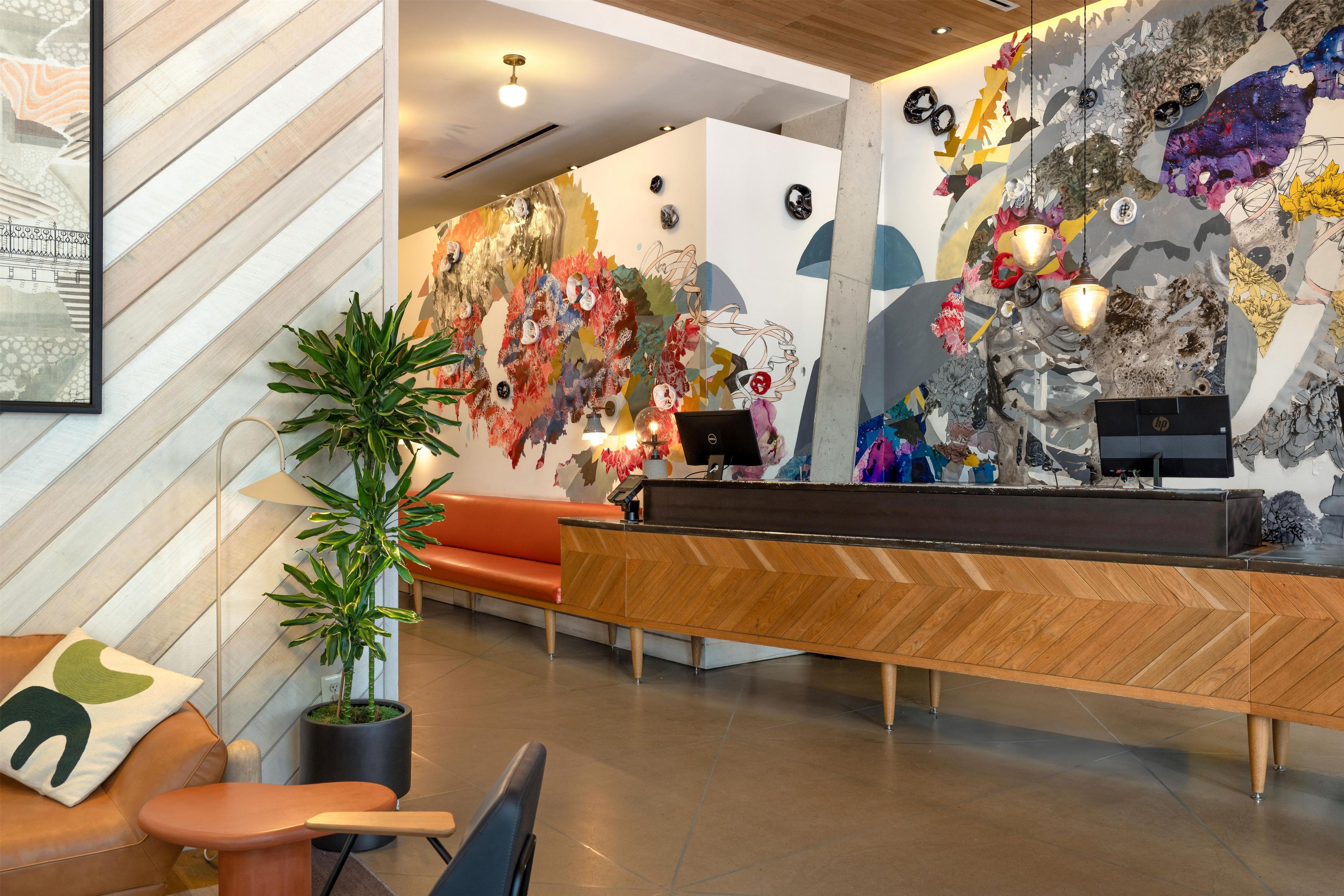 A reception area with a wooden reception desk, a potted plant, a sofa, and a wall with abstract art.