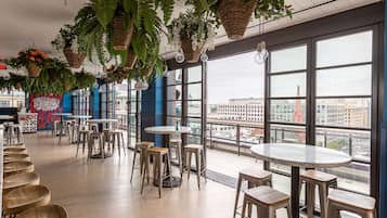 Un café moderno con plantas colgantes, ventanas amplias y vista a la ciudad.
