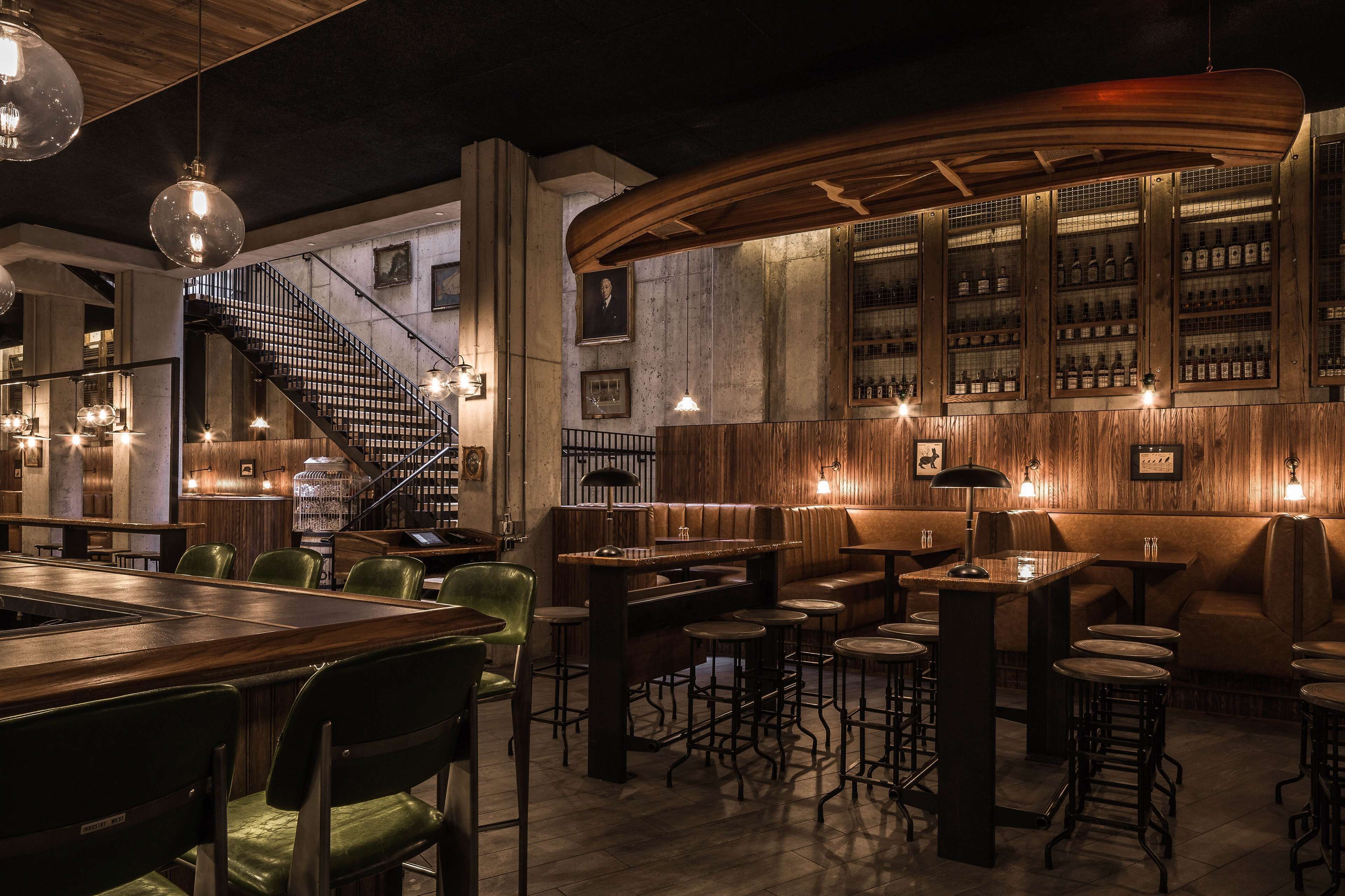 Een bar met houten meubels, een trap en een wand vol drankflessen.