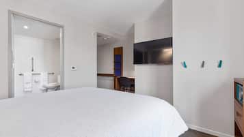 A bedroom with a large bed, a TV mounted on the wall, and a wooden dresser.