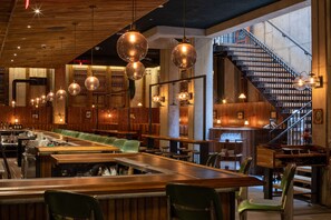 Een restaurant met een bar, houten plafond, hangende bolvormige lampen en een trap.