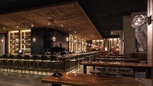 A bar area with wooden bar counters, bar stools, and hanging pendant lights. - Motto by Hilton Washington DC Downtown (Washington)