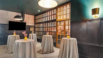 A room with multiple round tables, each with a tablecloth and a vase of flowers. There are two pendant lights hanging from the ceiling.