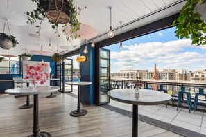 Una terrazza panoramica sul tetto con tavoli rotondi, piante pensili e vista sulla città.
