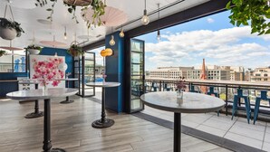 A rooftop terrace with round tables, hanging plants, and a city view. - Motto by Hilton Washington DC Downtown (Washington)