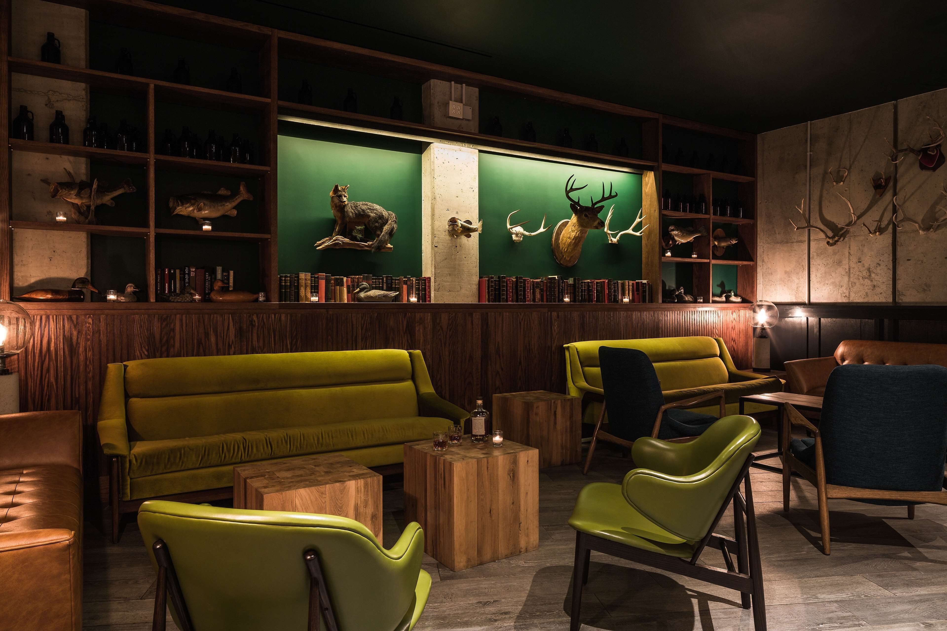Een kamer met een groene wand, houten planken met diverse spullen, een groene bank en groene stoelen.
