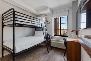 A bunk bed room with a desk and chair, a window with a view, and a heater.