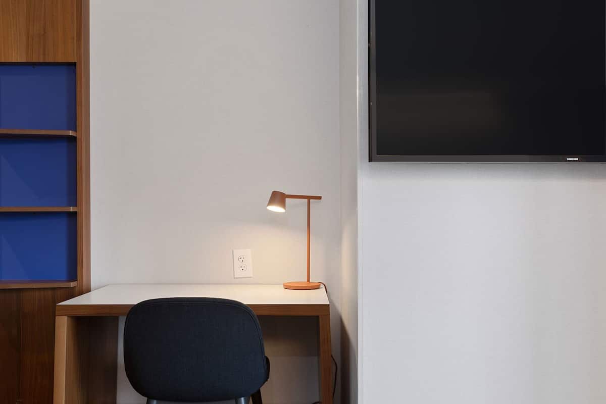 Ein Schreibtisch mit Lampe, ein Stuhl und ein an der Wand montierter Fernseher.