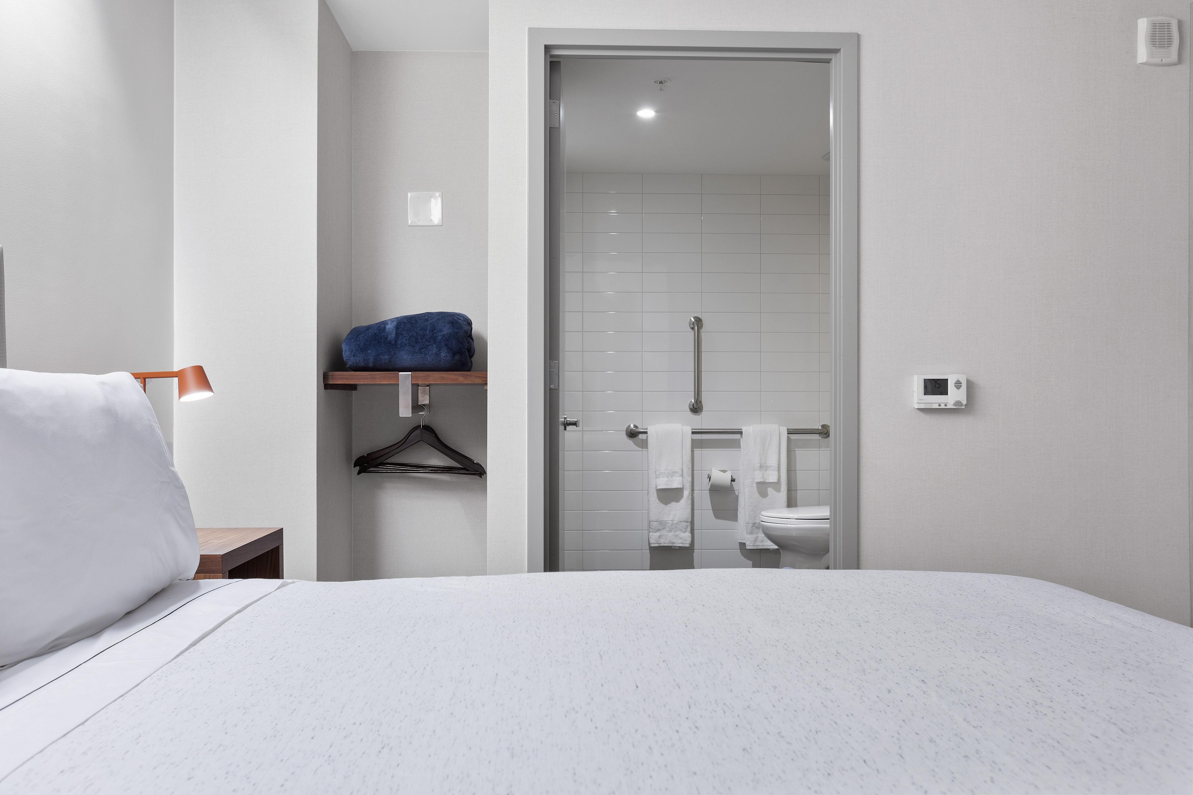Habitación de hotel con cama, toallero con toalla, estante pequeño, inodoro y zona de ducha.
