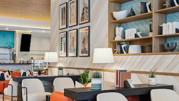Un lobby de hotel moderno con zona de comedor, obras de arte enmarcadas en la pared y una estantería con libros y objetos decorativos.
