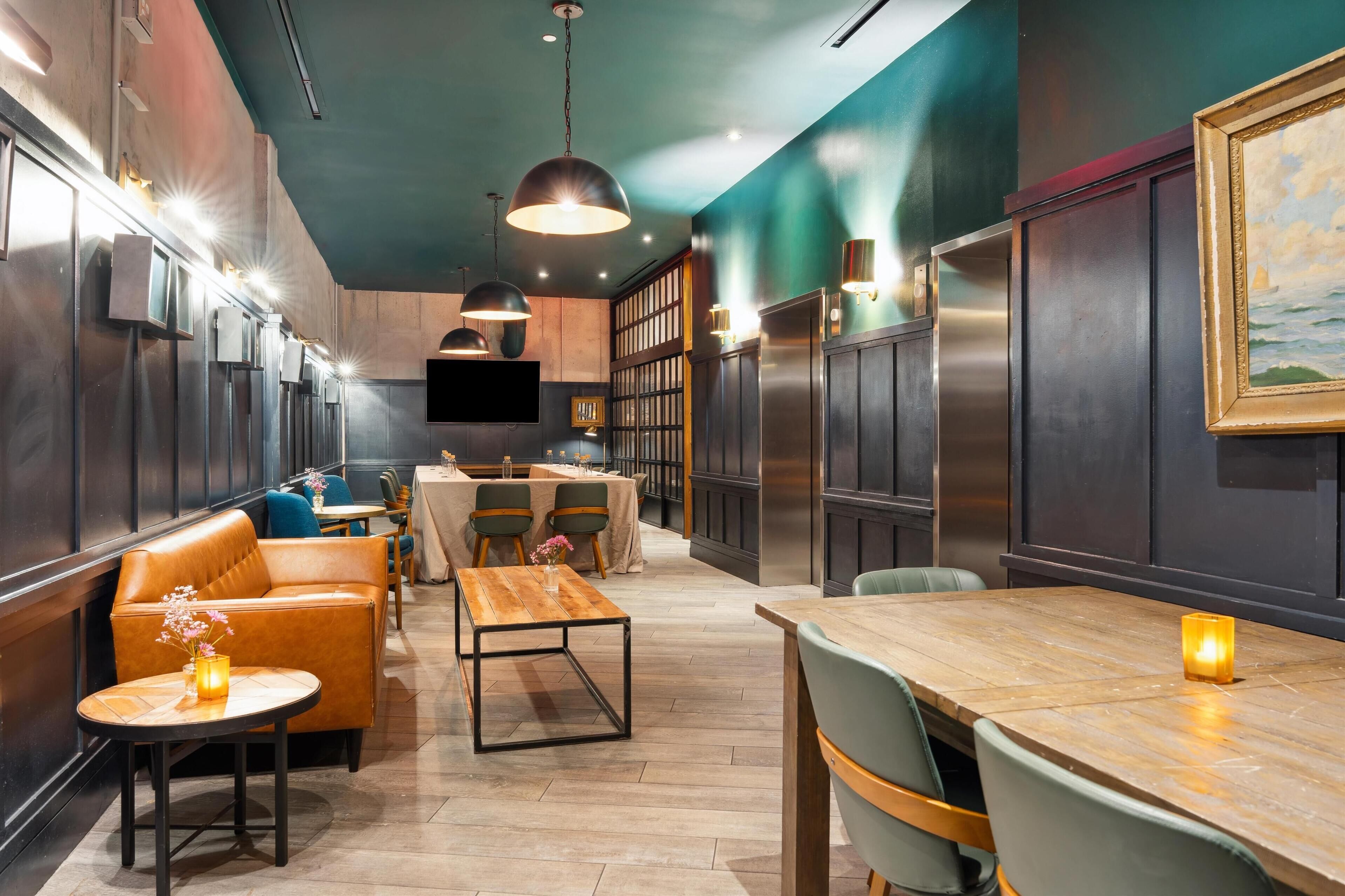 A modern restaurant interior with leather seating, wooden tables, pendant lighting, and a view of the kitchen.