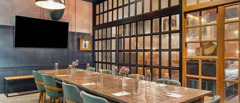 A conference room with a long wooden table, six chairs, and a large window with a view of the city.