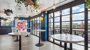 A spacious room with large windows, multiple tables, hanging plants, and a view of the cityscape.