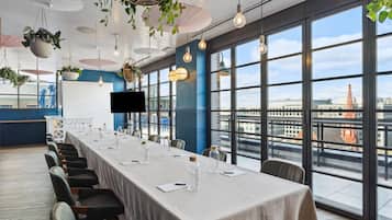 Un salón de conferencias con una larga mesa, sillas y vistas a la ciudad a través de amplios ventanales.