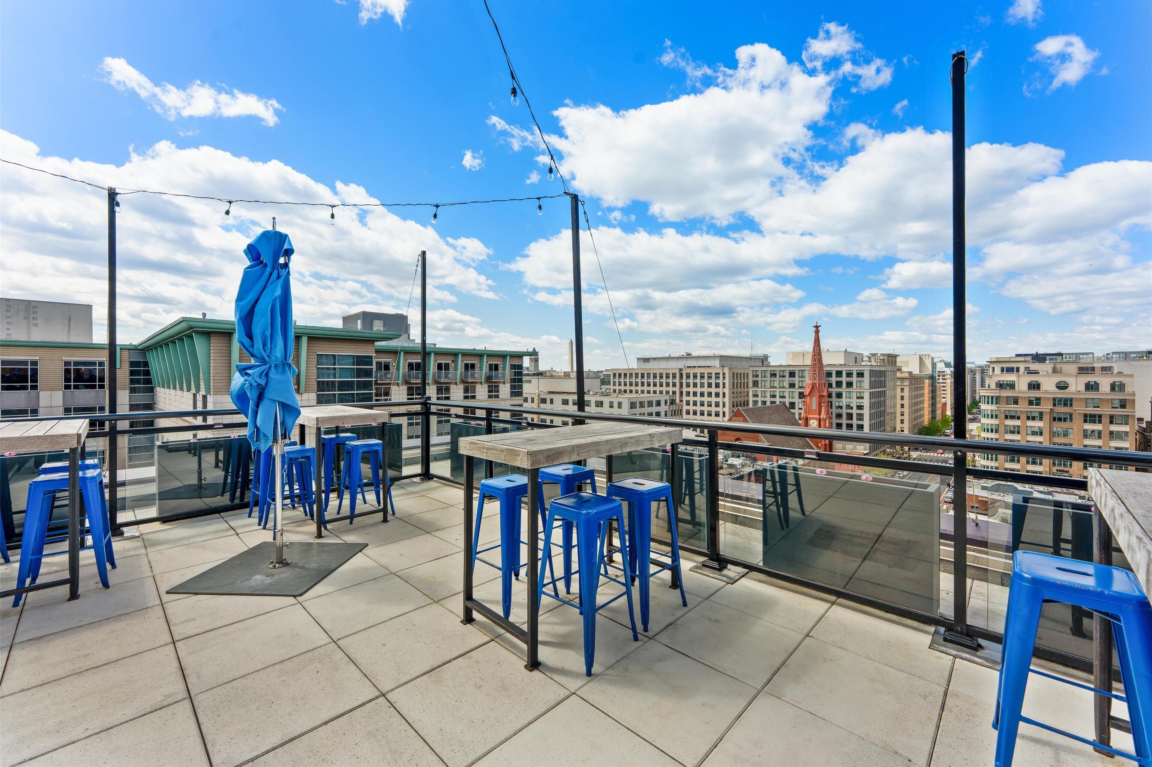 Una terraza en la azotea con taburetes azules, una mesa de madera y una gran escultura azul.