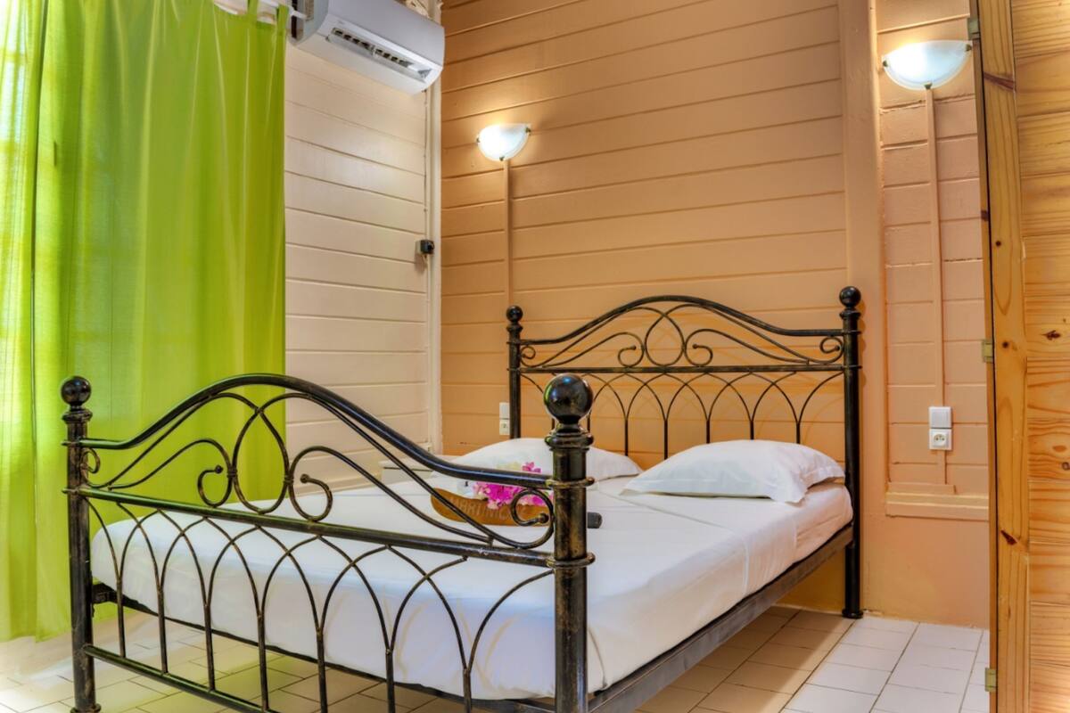 Ein Einzelbett mit Metallgestell in einem Zimmer mit Holzwänden und einem grünen Vorhang.