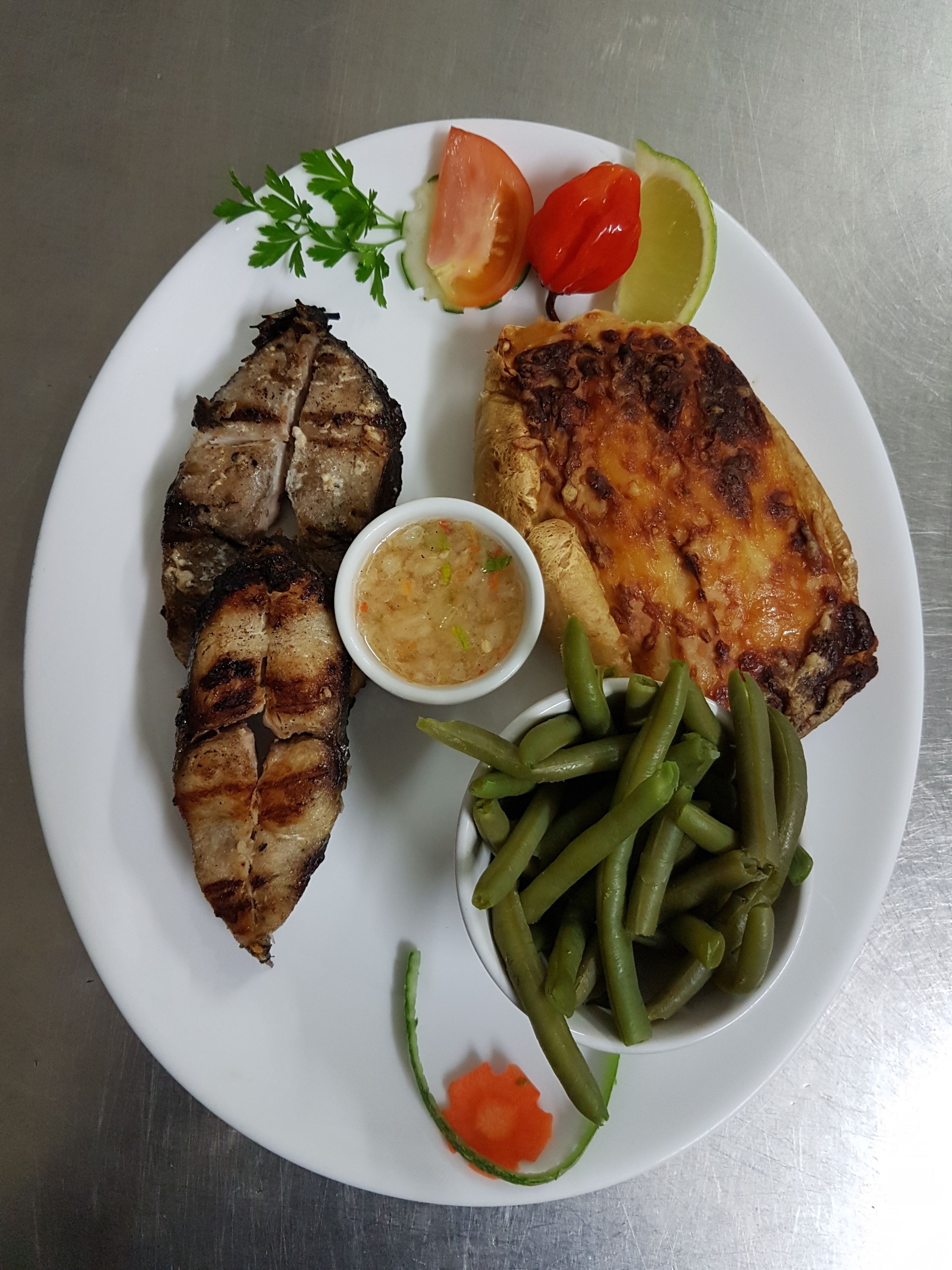 Une assiette contenant de la viande grillée, des haricots verts, une tranche de tomate, une tranche de citron vert et un petit bol de sauce.