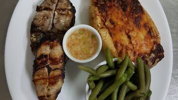 Une assiette contenant de la viande grillée, des haricots verts, une tranche de tomate, une tranche de citron vert et un petit bol de sauce.