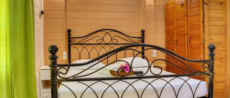 A metal-framed bed with white bedding, a green curtain, and wooden walls with a wooden wardrobe.