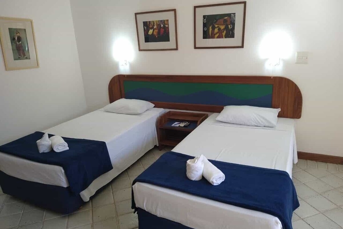 Una habitación de hotel con dos camas individuales, un cabecero de madera y dos cuadros en la pared.