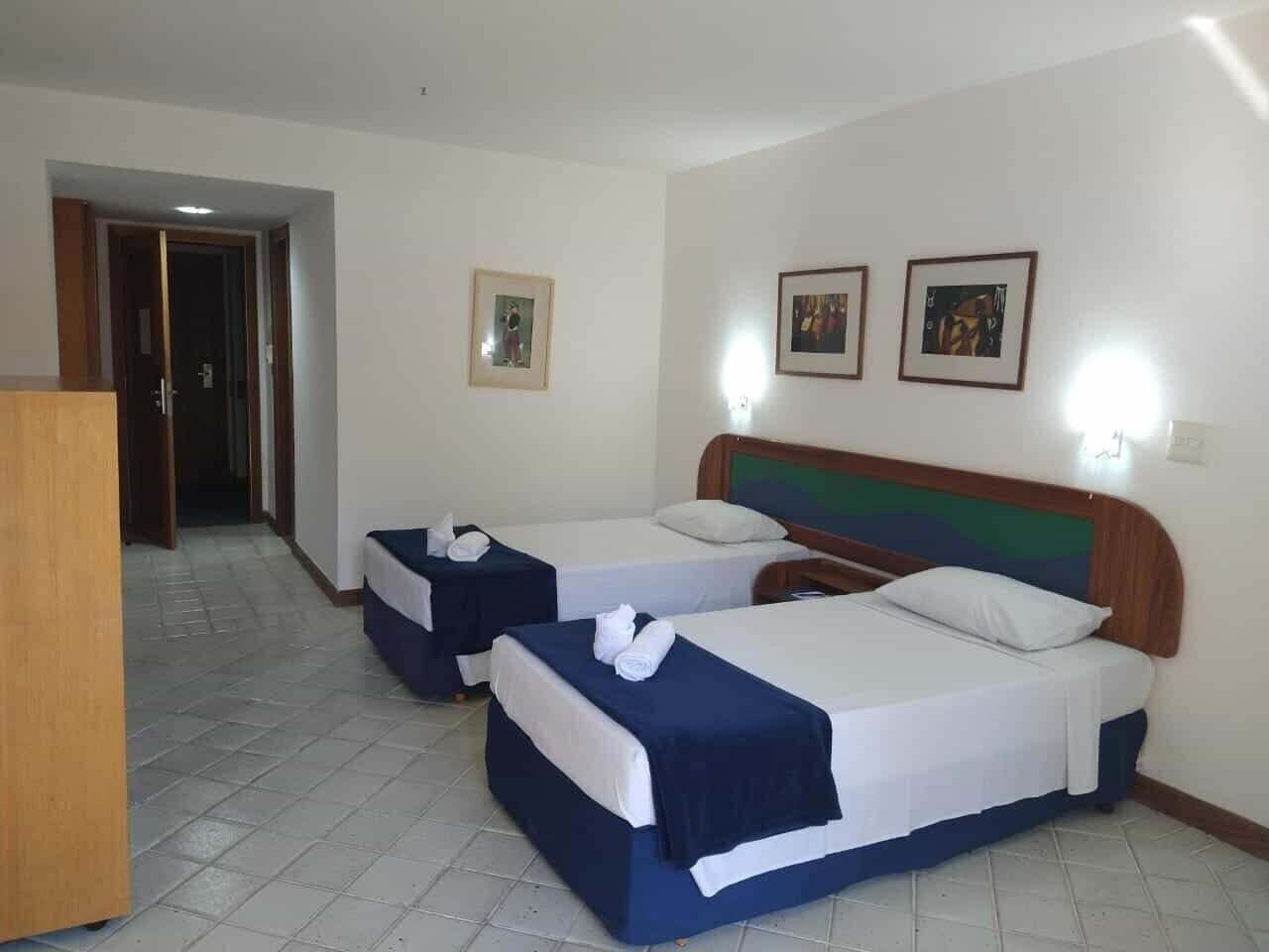 Quarto de hotel com duas camas, um painel de cabeceira de madeira e uma escrivaninha.