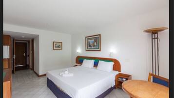 A hotel room with a bed, a bedside table, a chair, a lamp, and a picture on the wall.