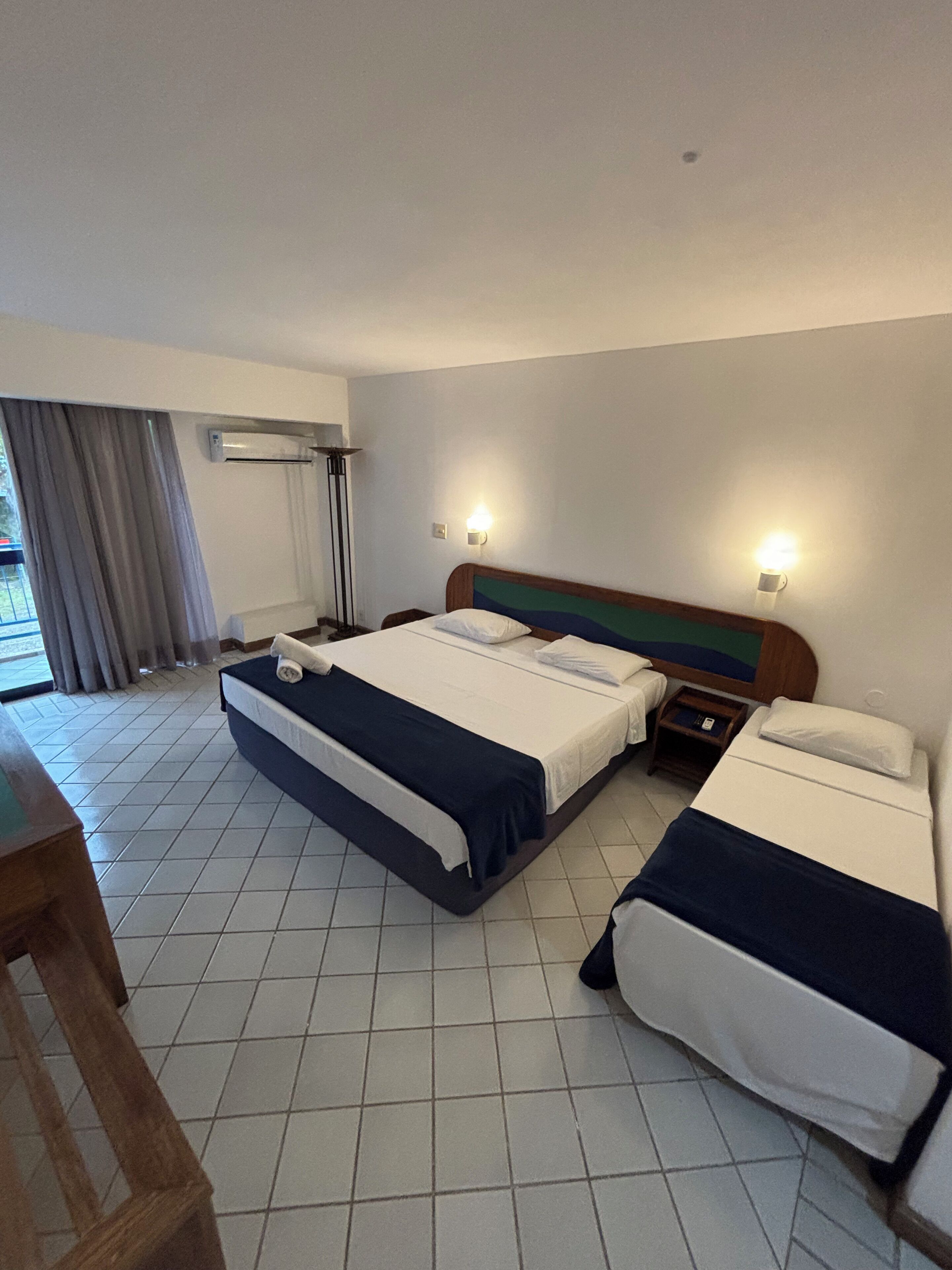 Habitación de hotel con dos camas, un escritorio y una ventana con cortinas.