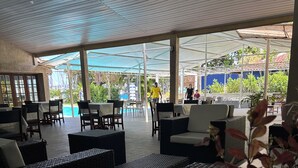 Zona de estar exterior con mobiliario de mimbre y sombrillas, con vista a una piscina y follaje.