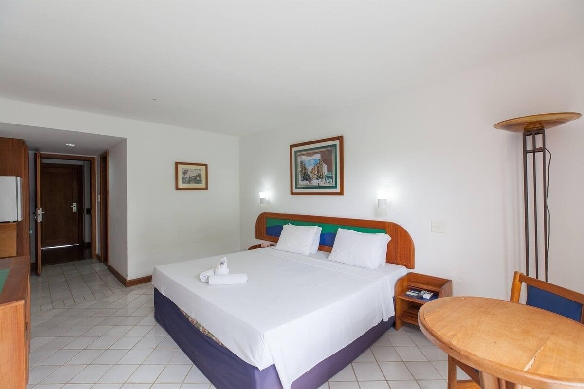 Una habitación de hotel con cama, mesita de noche, sillón, escritorio y lámpara.