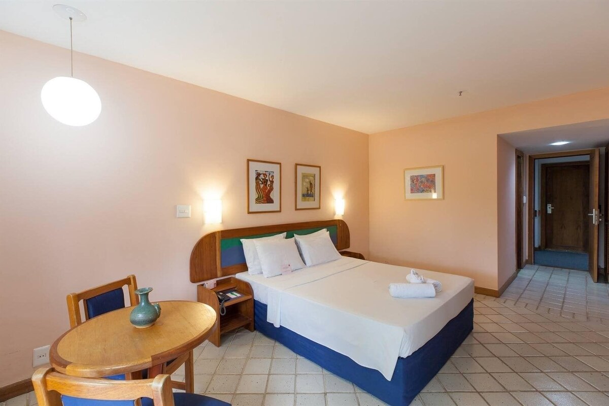 A hotel room with a bed, bedside table, chair, and artwork on the walls.