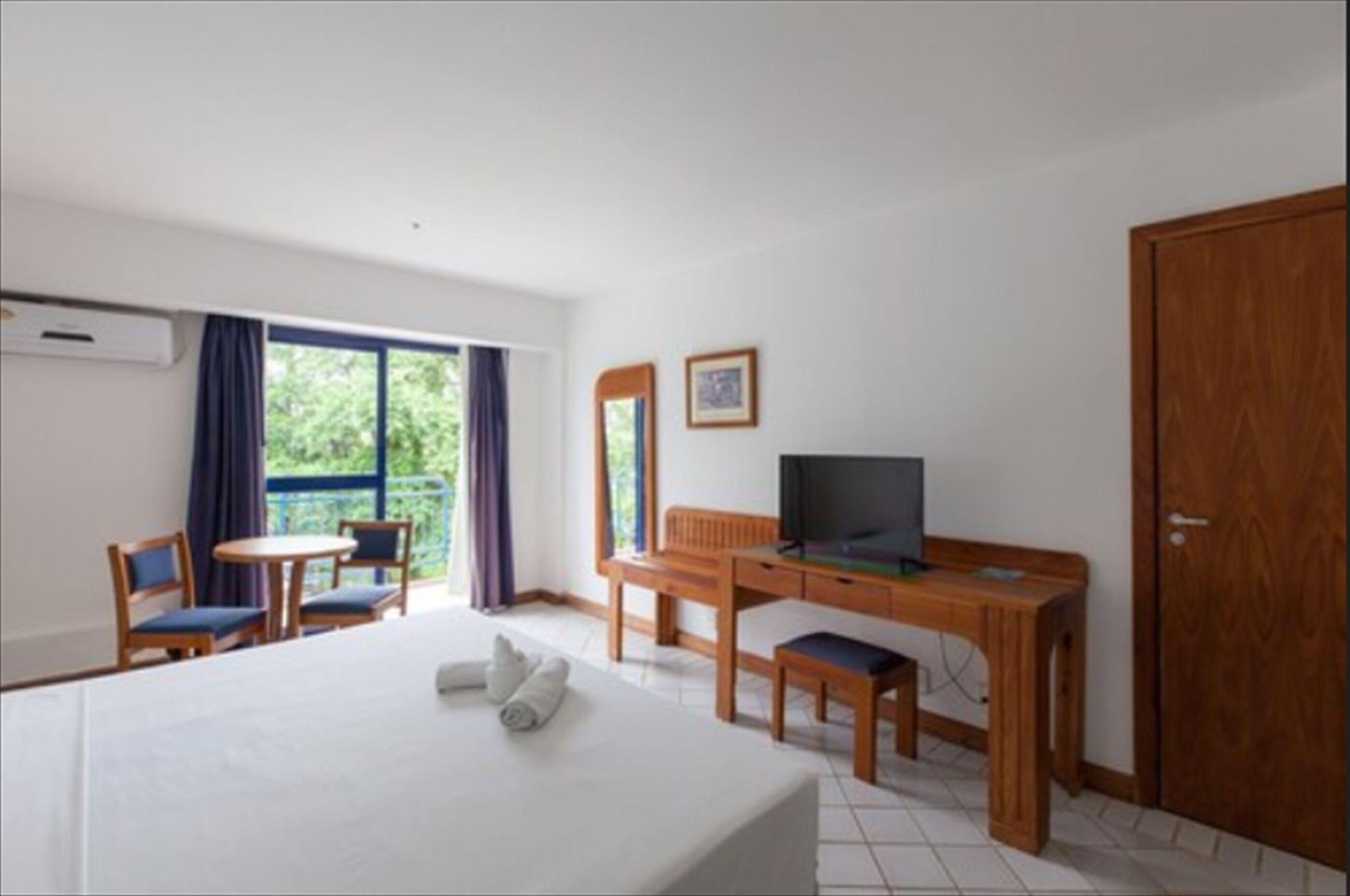 A hotel room with a bed, a desk with a TV, a chair, a small table, and a wardrobe.